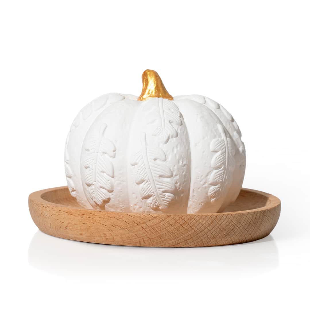 White plaster pumpkin diffuser with embossed leaves and gold stem on a light beech wood tray against white background