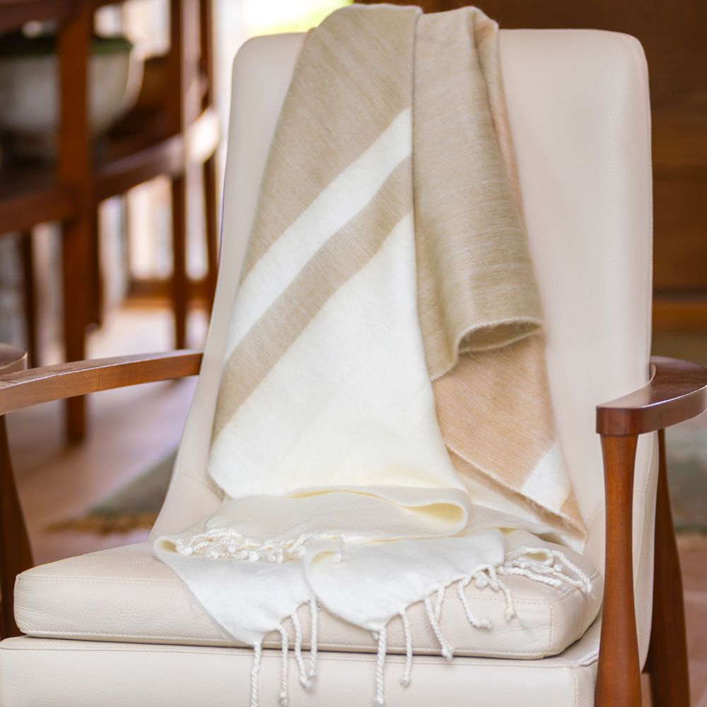 Tobacco and wheat striped alpaca throw draped over a cream leather armchair with twisted fringe