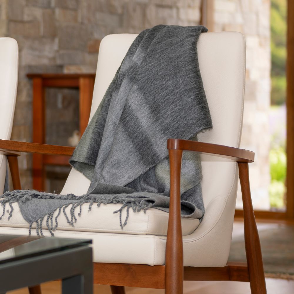 Gray and olive striped alpaca throw draped over a mid-century modern chair with white upholstery