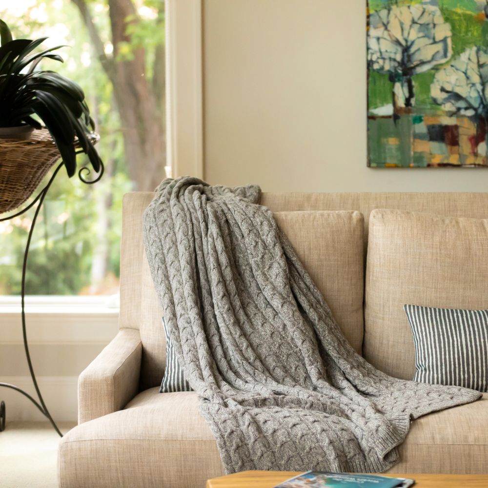 Graphite gray cable knit throw draped on beige sofa with striped pillows