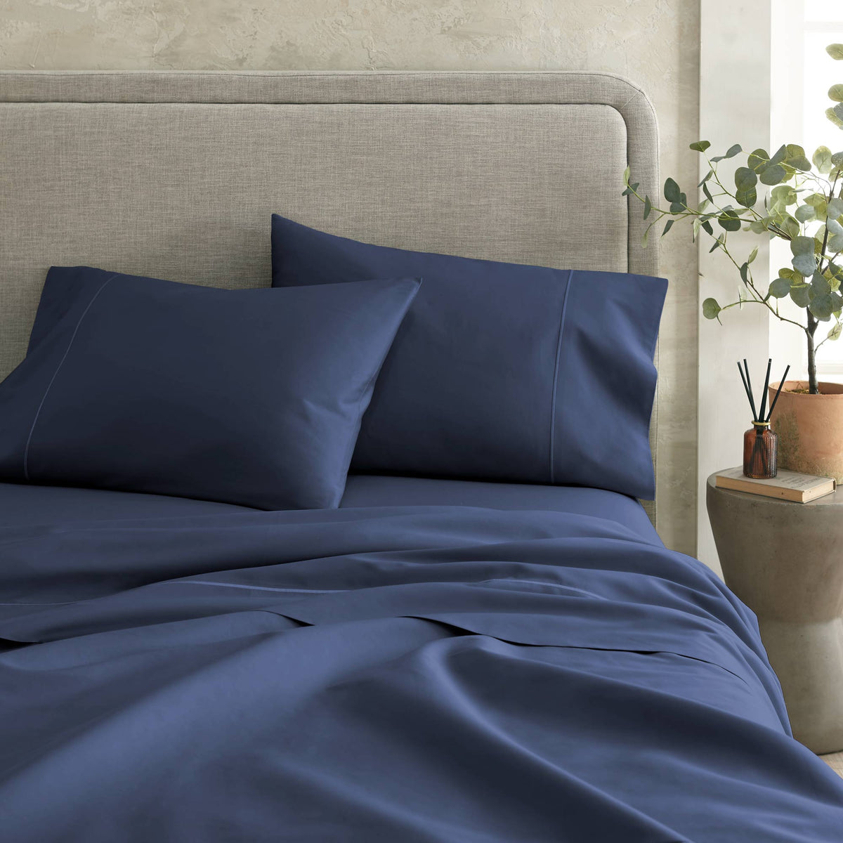 Deep navy blue sateen bedding set styled on a bed with grey headboard and side table decor