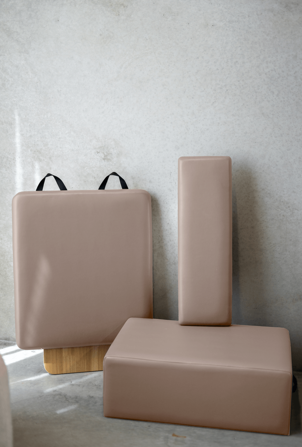 Dusty rose Pilates accessories set including box, platform, and block against concrete wall
