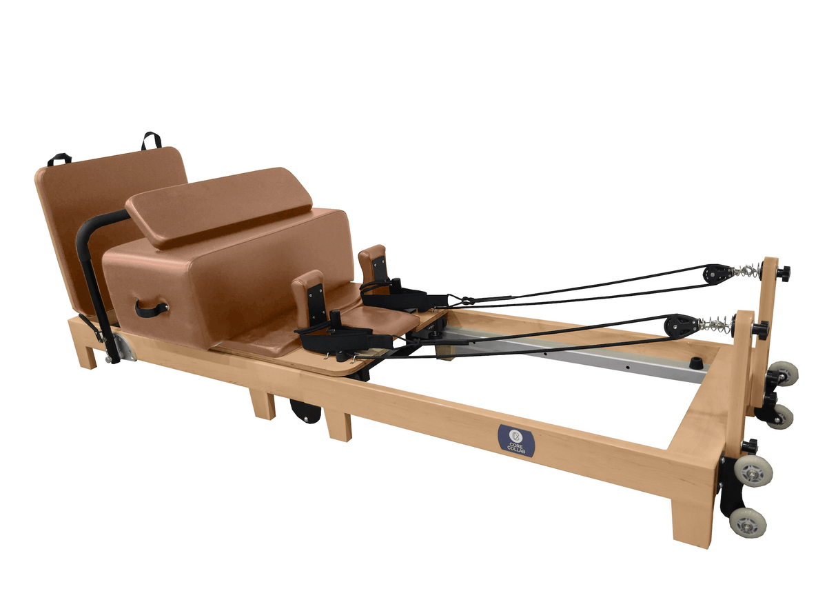 Tan leather reformer with FSC oak frame, six springs, foot straps, and mobility wheels on white background
