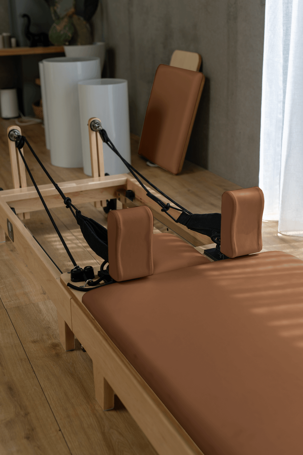 Sunlit close-up of tan leather platform, padded blocks, black ropes, and detached backrest in studio