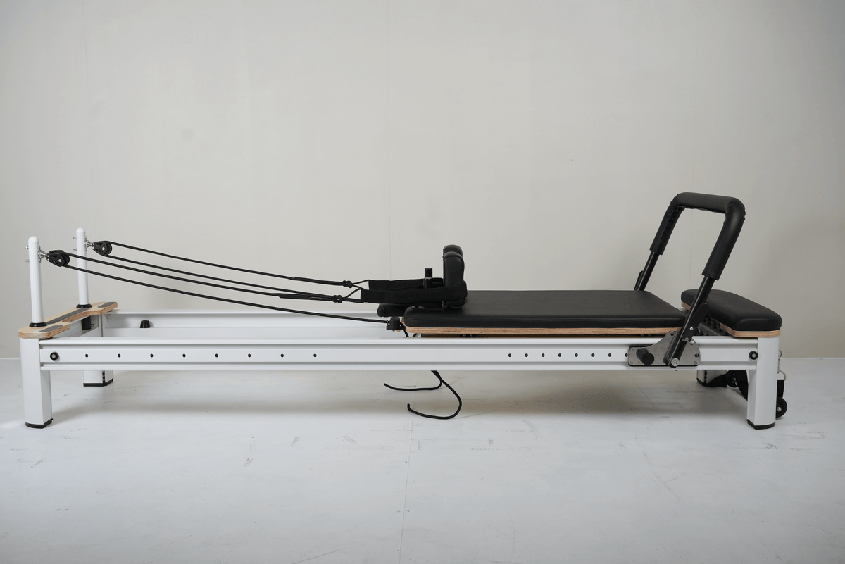 Side view of white aluminum Core Collab reformer with black leather carriage, wood footbar, and matte black handlebar.