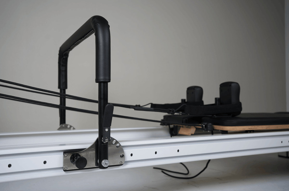 Close-up of black padded handlebar attached to white rail via stainless steel bracket with tensioned black ropes.