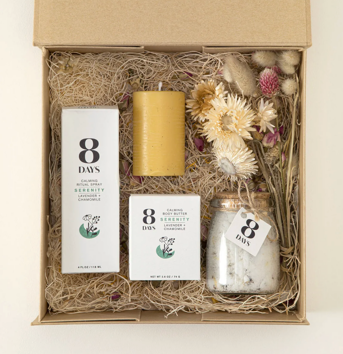 Open gift box filled with kraft paper showing boxed body butter, ritual spray, yellow candle, and dried wildflower bundle