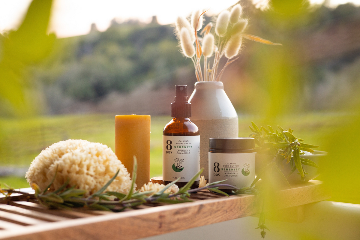 Serenity collection on slatted tray featuring amber spray bottle, white body butter, yellow candle, sea sponge, and bunny