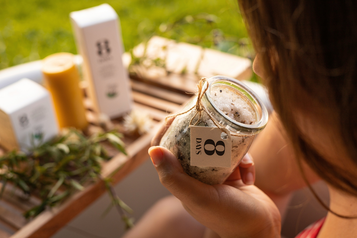 Woman holding glass jar of mineral-rich bath salts mixed with dried lavender and chamomile herbs sealed with twine tag