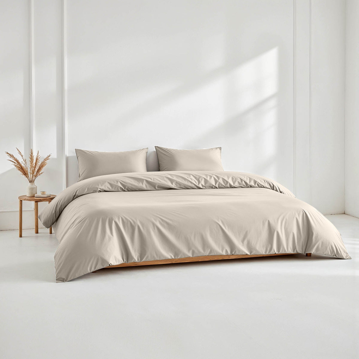 Warm taupe sateen bedding set arranged on a low wooden platform bed in a minimalist white room