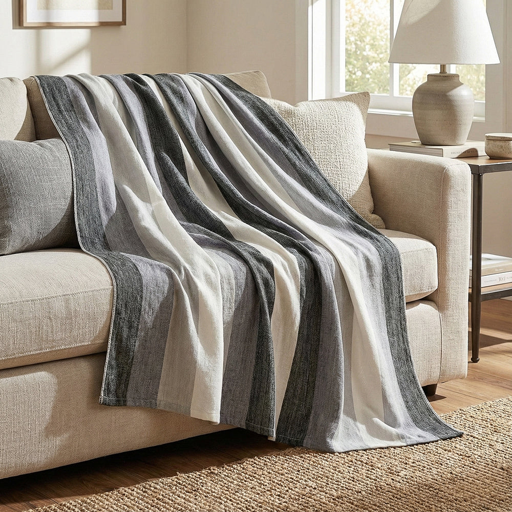 Black, gray and white striped alpaca throw blanket draped over a beige sofa in a sunlit room