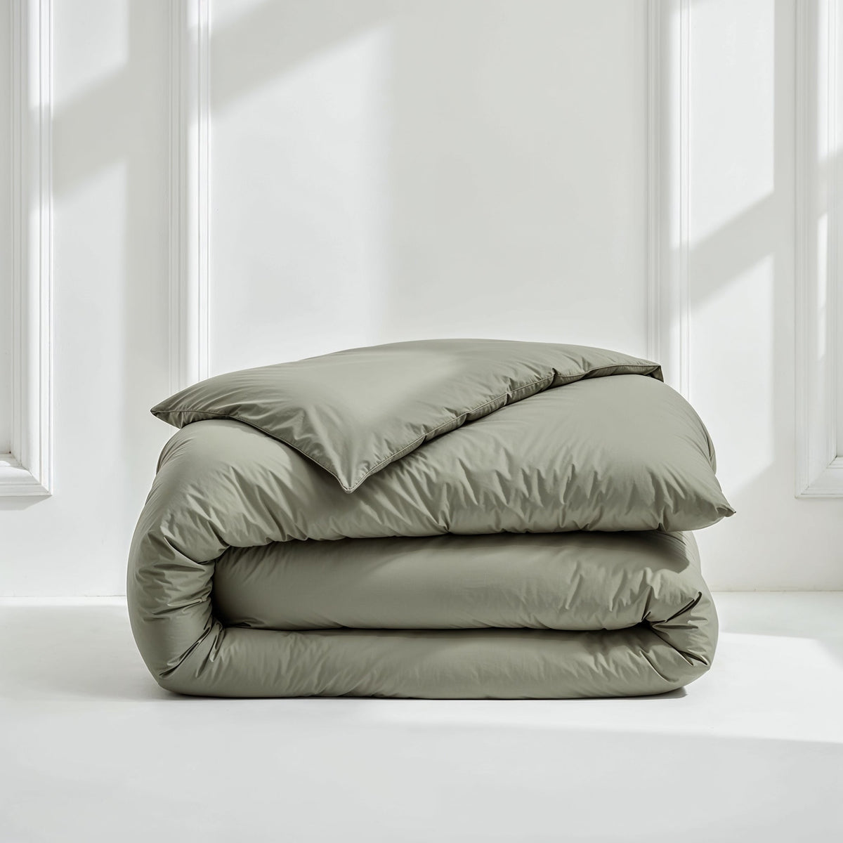 Stacked sage green sateen duvet cover on white surface under natural light