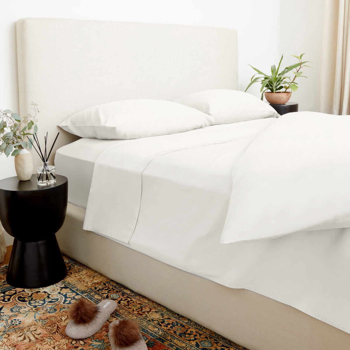 Crisp white sheets and duvet cover on a beige upholstered bed styled with a black side table