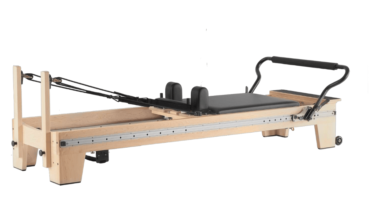 Side view of a wooden pilates reformer machine with black carriage and metal rails on white background