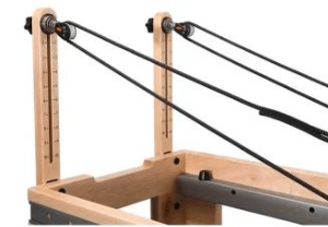 Close-up of wooden tower showing dual pulley wheels and black resistance cables for pilates reformer machine