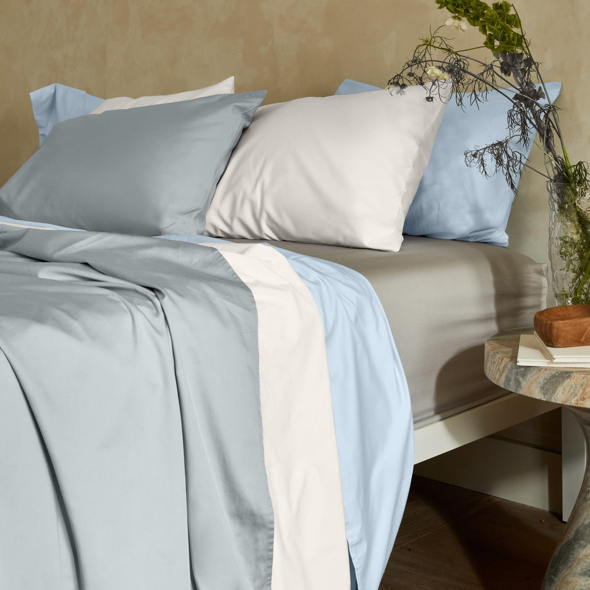 Multi-tone color-block bedding with wide vertical stripes arranged on a bed with a marble side table