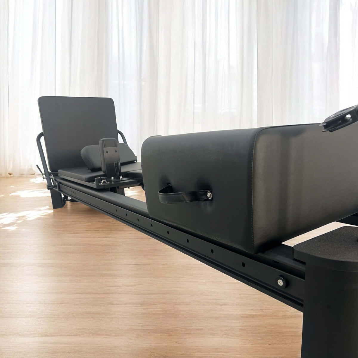 Perspective view of reformer spring box, black leather handle, textured upholstery, and perforated aluminum rail.