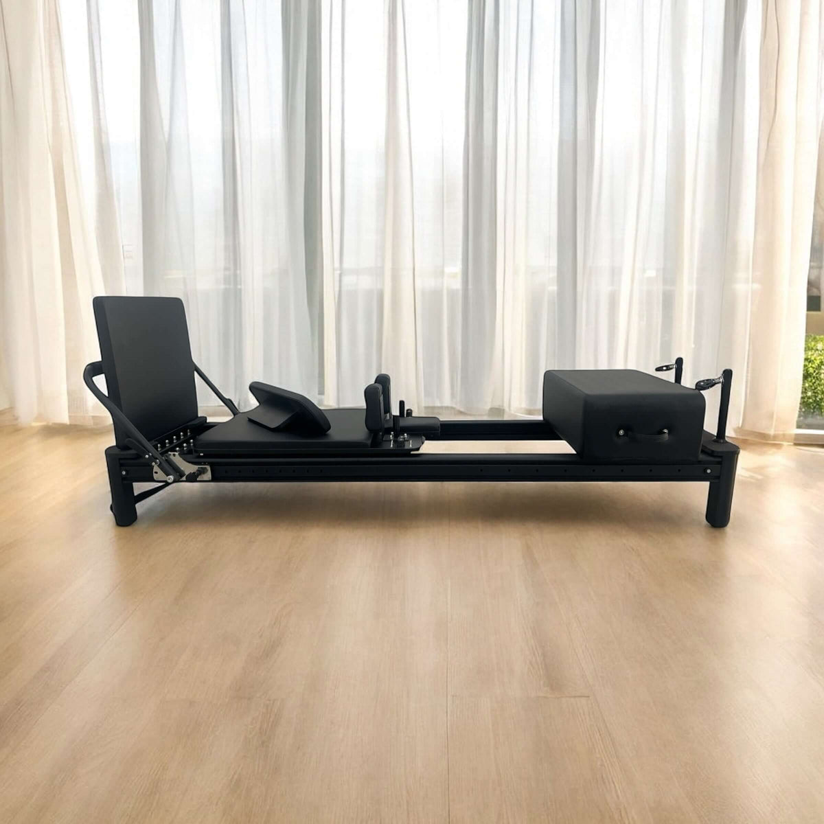 Full eye-level shot of matte black Full Track Queen reformer on light wood flooring in a bright studio.