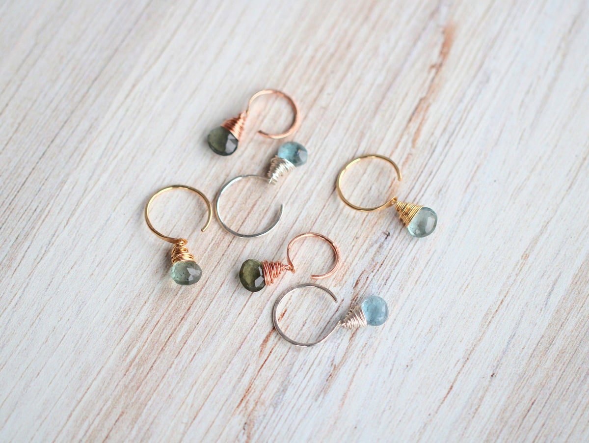 Flat lay of mixed metal huggies with varying shades of faceted moss aquamarine