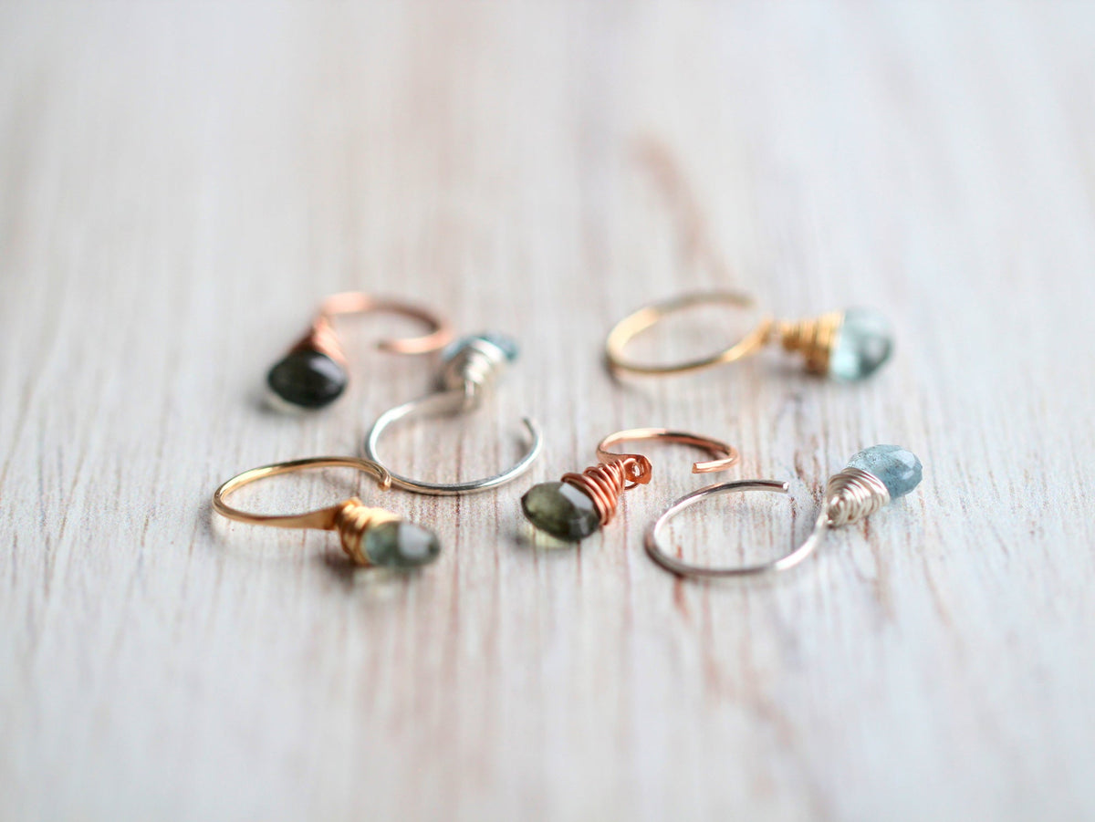 Angled view of scattered silver, gold, and rose gold hoops with green-blue gems