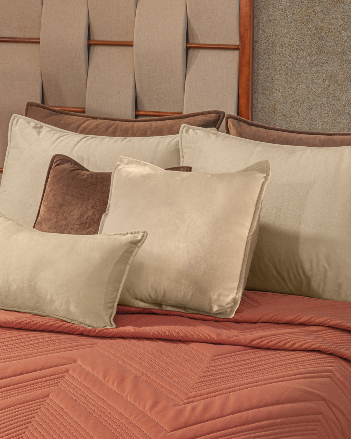 Close-up of plush cream and brown velvet throw pillows arranged on textured terracotta quilted bedspread stitching