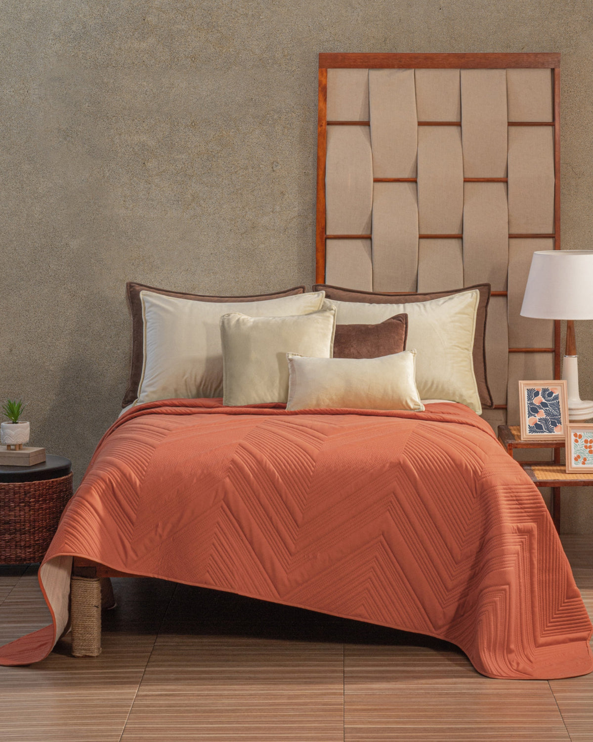 Full view of terracotta chevron bedspread on a bed with woven wooden headboard and mixed neutral pillows near botanical art