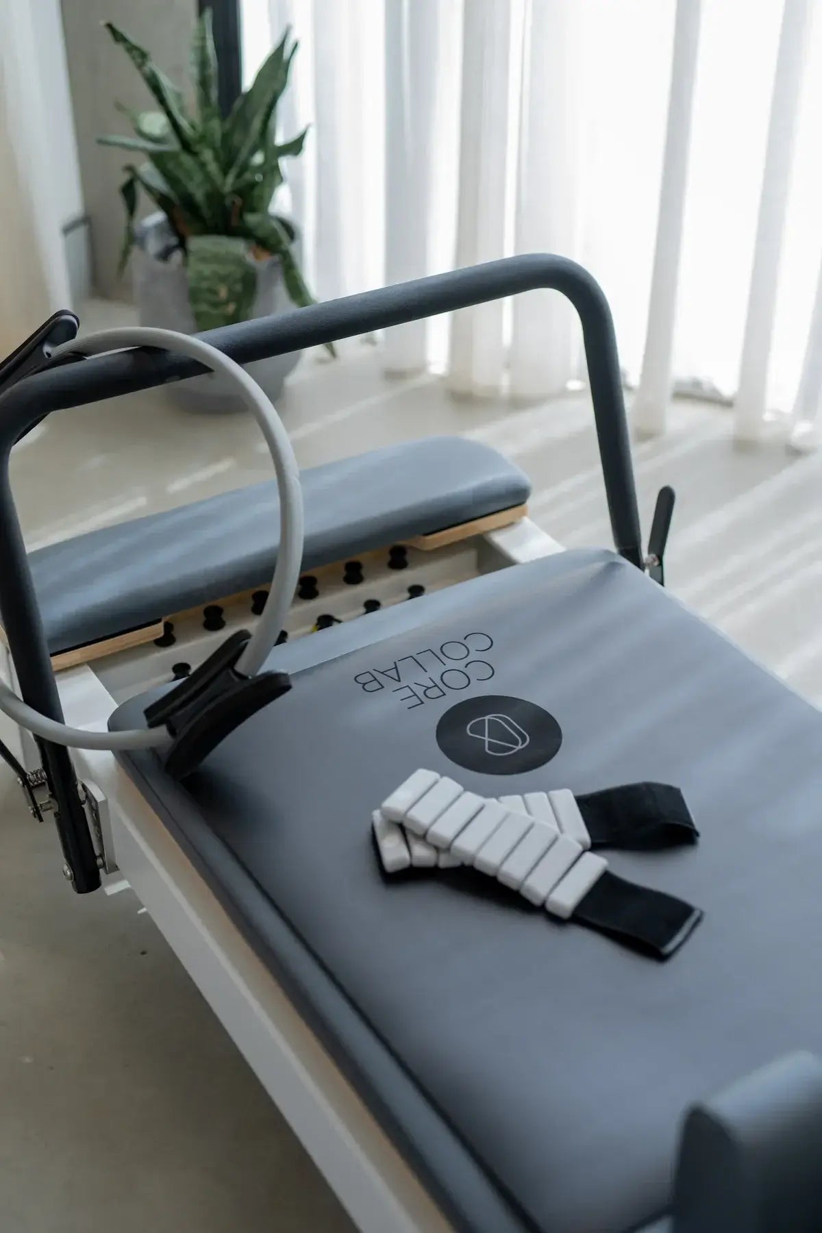 Close-up of grey exercise ring hooked on reformer footbar next to white segmented wrist weight with CORE COLLAB logo