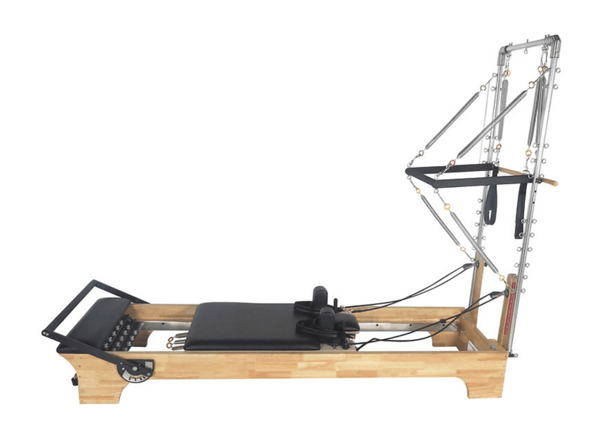 Side view of light wood pilates reformer with tower, black carriage, silver springs, and straps on white background