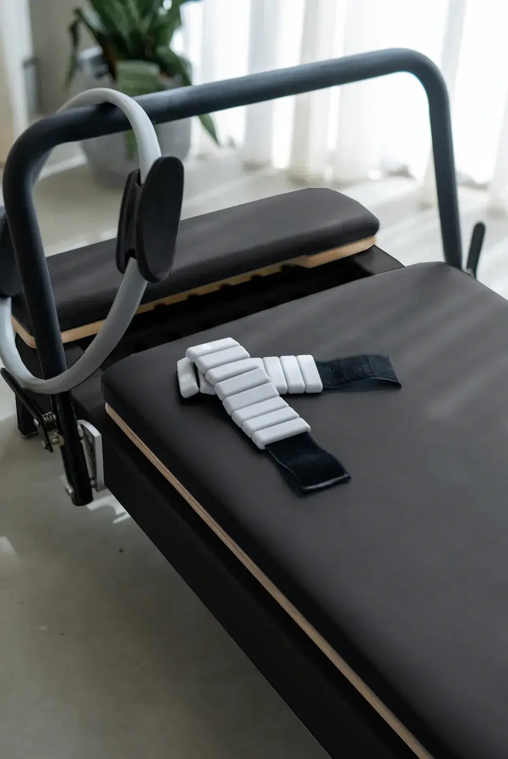 Grey Pilates ring hooked on handle with weighted strap on black padding