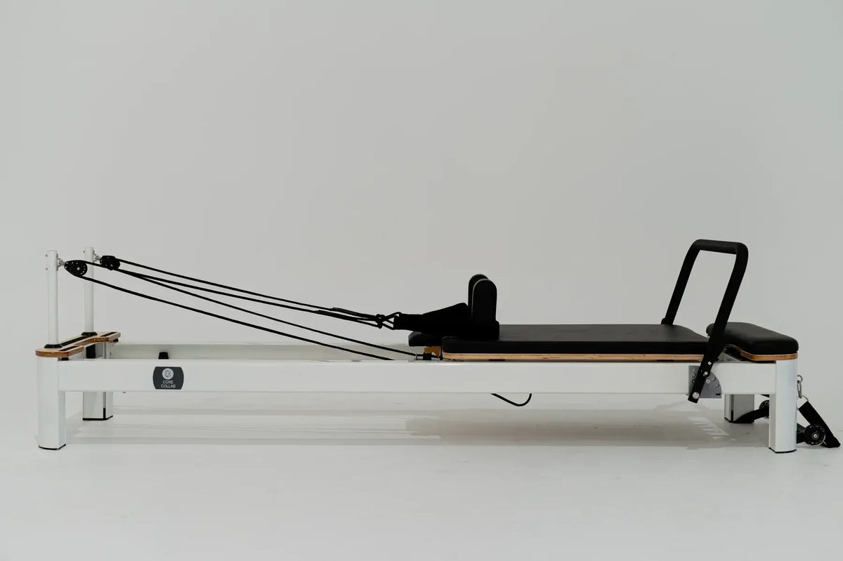 Side profile of white Pilates reformer with black carriage against white background