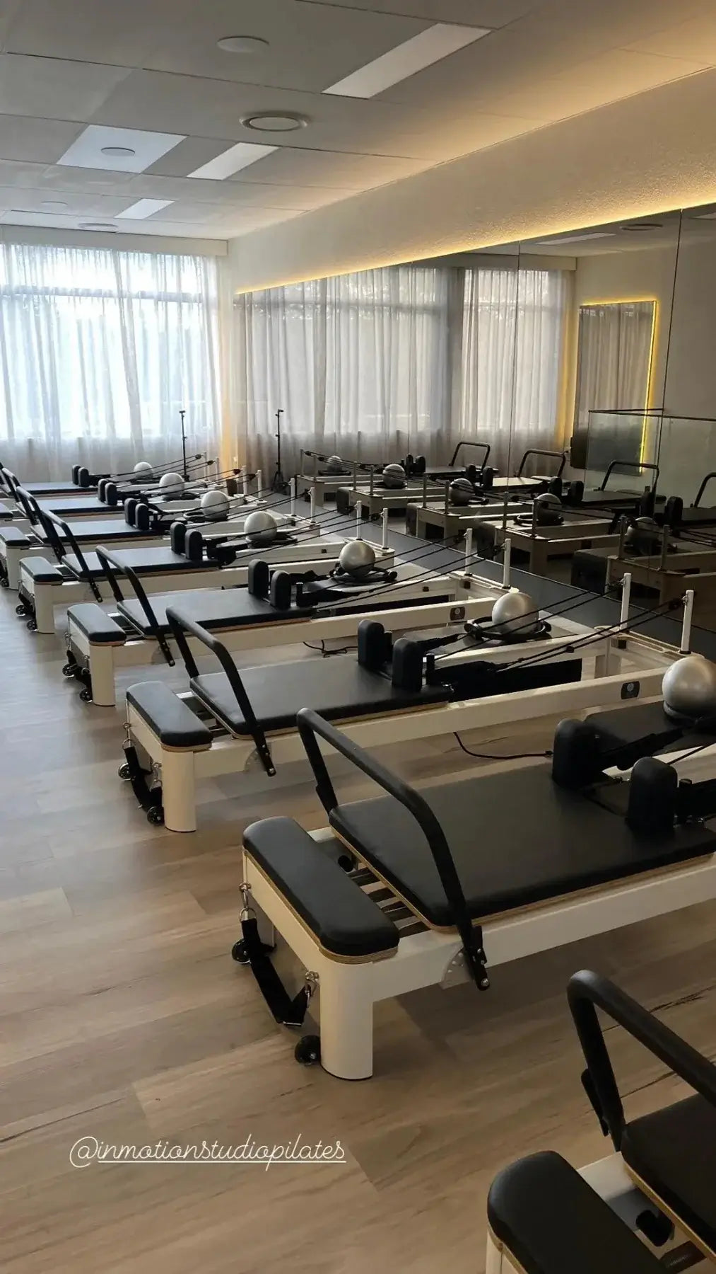Rows of white Pilates reformers arranged in professional studio facing mirror