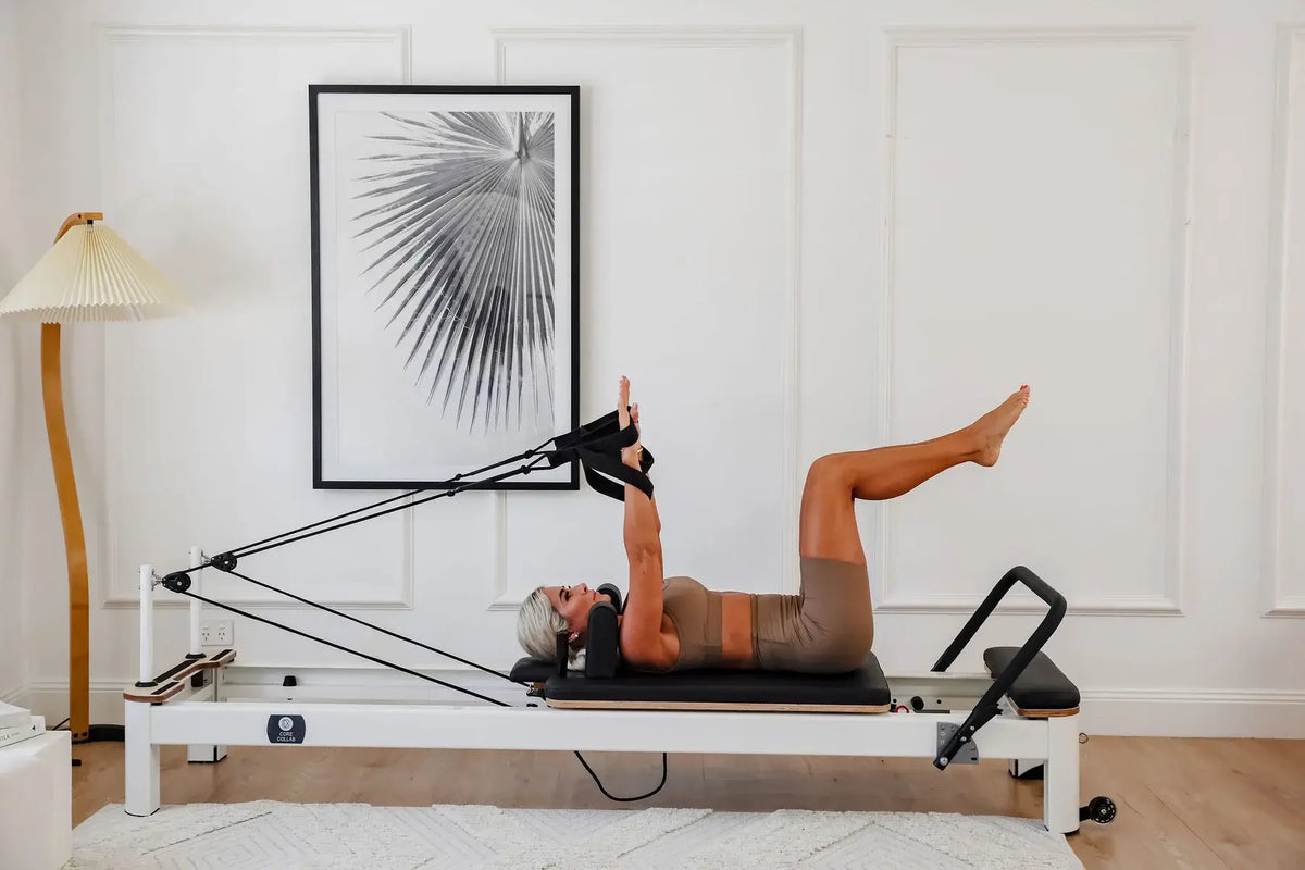 Woman using rope handles on white Pilates reformer in bright home studio