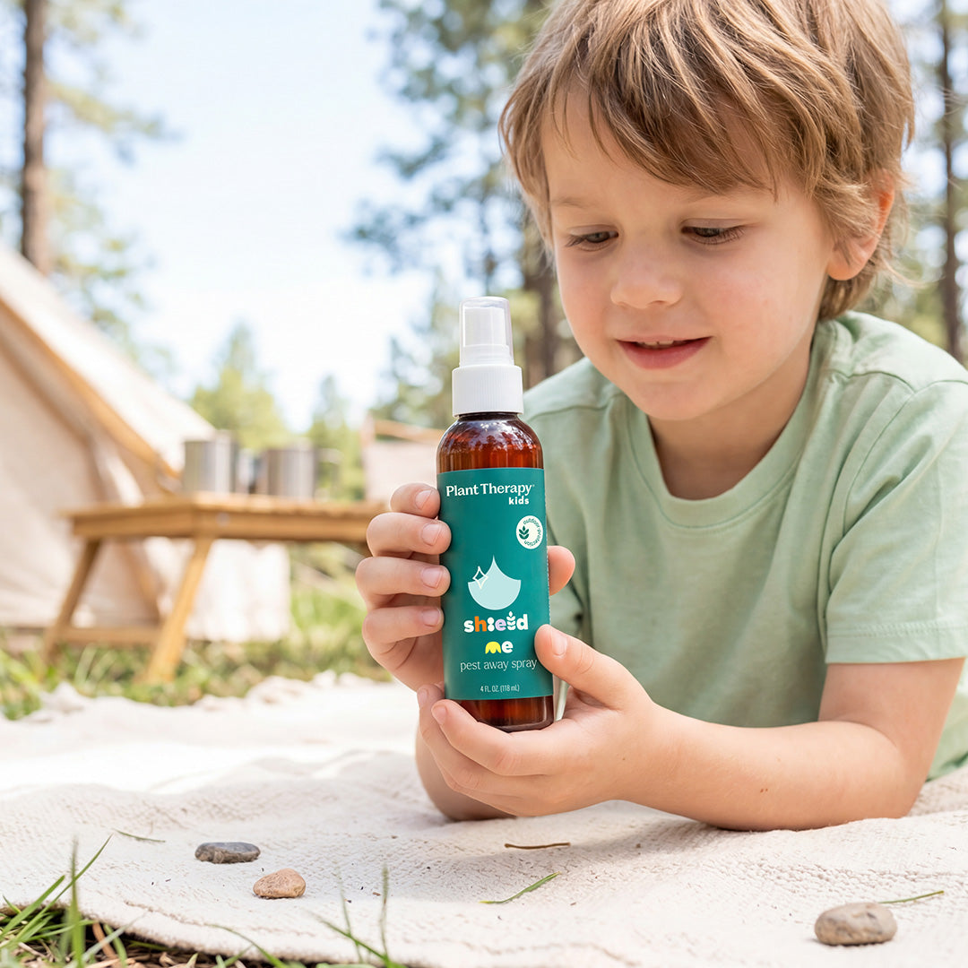 Young boy in green shirt holding amber spray bottle while lying on outdoor blanket near tent