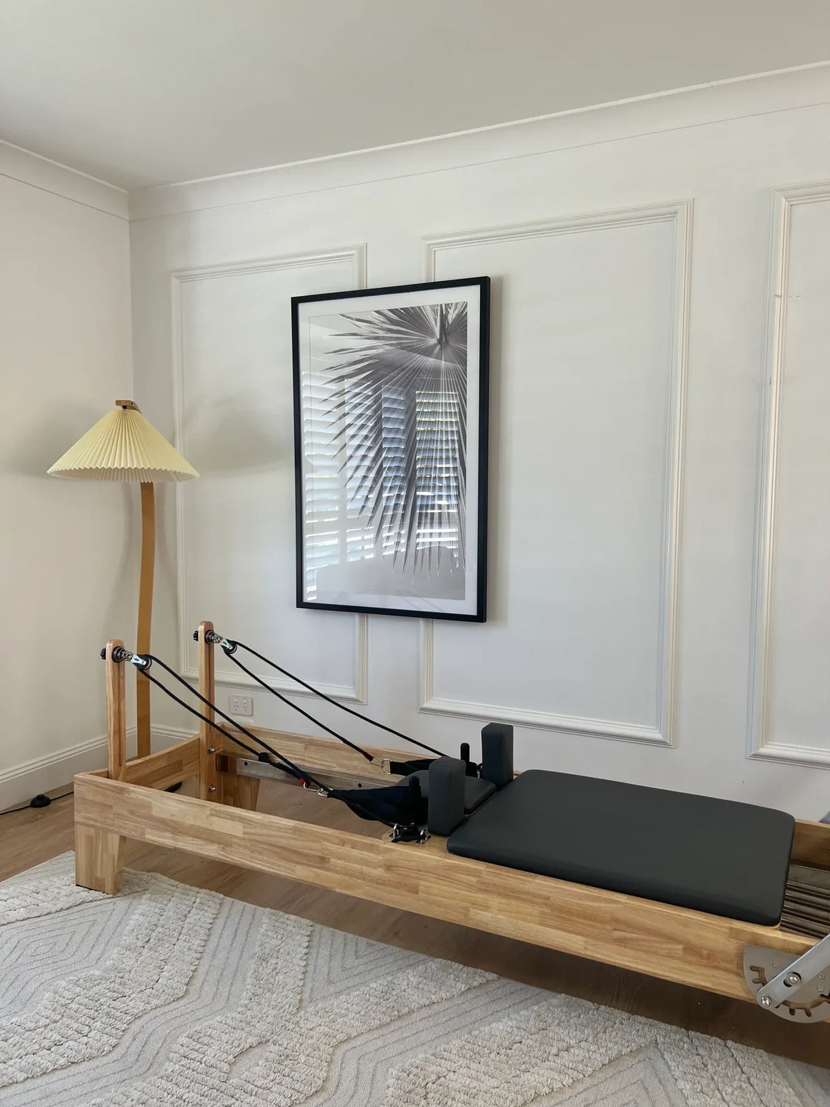 Full shot of luxury minimalist pilates reformer in bright home studio with white wainscoting and textured rug