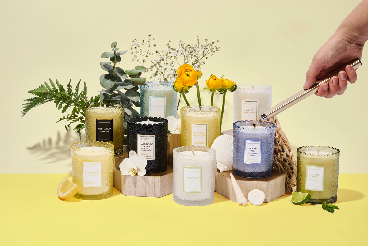 Colorful candles on wooden blocks with eucalyptus, citrus slices, and shells against yellow background