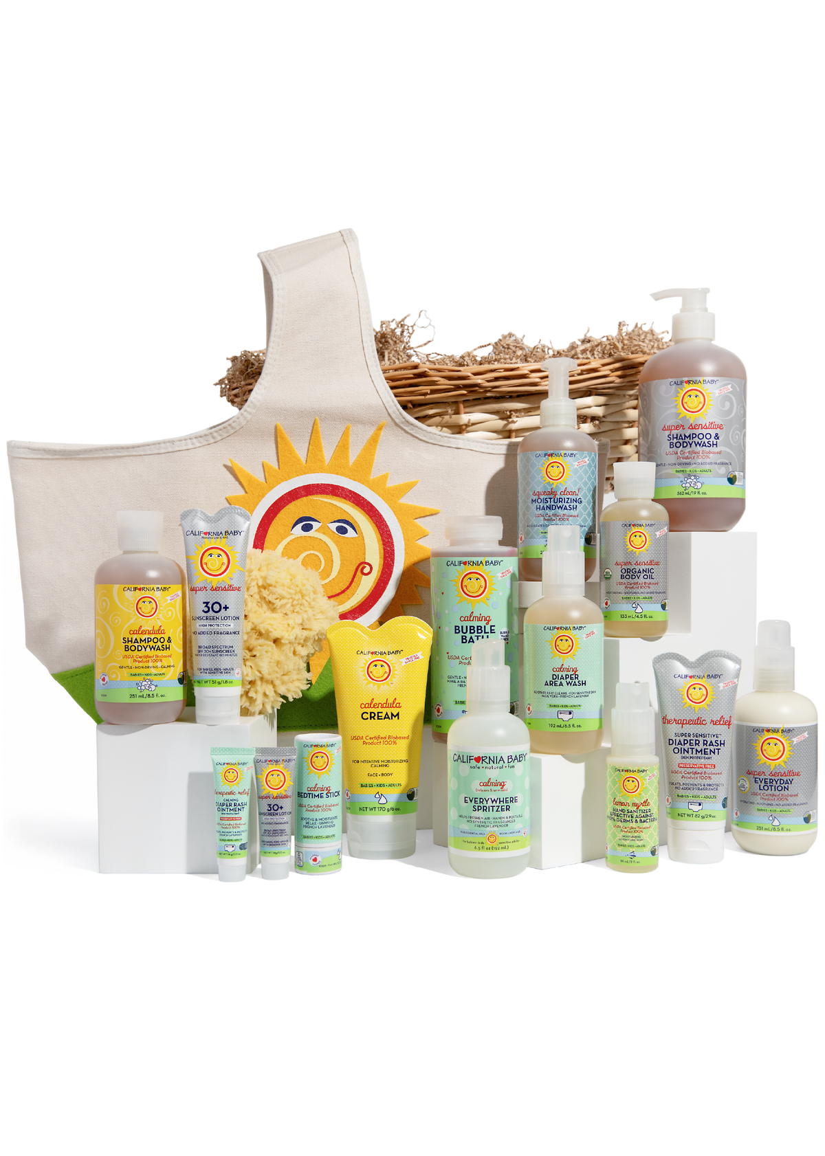 California Baby gift set on white pedestals with wicker basket and cream tote featuring embroidered sun logo